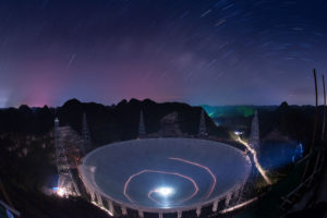 In this photo released by China's Xinhua News Agency, a vehicle leaves light trails in a long exposure photo as it drives beneath the Five-hundred-meter Aperture Spherical Telescope (FAST) in Pingtang County in southwestern China's Guizhou Province Monday, June 27, 2016. Construction on the 500-meter (1600-feet) diameter radio telescope, which began in 2011, is nearing completion. (Liu Xu/Xinhua via AP) 